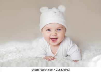 A portrait of a cute newborn baby in a white like a bear cub hat lying on its stomach and laughing