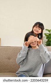 Portrait, Cute And Playful Young Asian Girl Surprising Or Playing Peek A Boo With Her Mom In The Living Room. Happy Family Concept