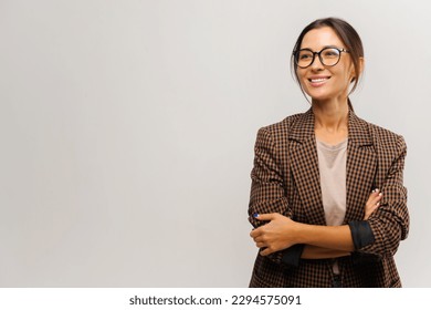 Portrait of cute positive businesswoman wearing formal suit standing with crossed arms and looking away with charming smile. Indoor studio shot isolated on white background - Shutterstock ID 2294575091