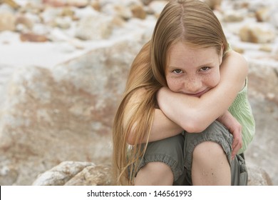 Portrait of cute preteen girl sitting on rock at beach