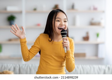 Portrait of cute pretty long-haired korean girl teenager singing at home, using microphone and gesturing, looking at copy space. Child singing karaoke, domestic entertainment for kids concept - Shutterstock ID 2114898239