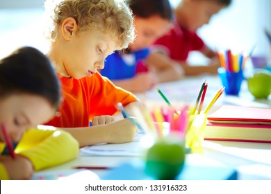 Portrait of cute schoolboy drawing at workplace among his classmates - Powered by Shutterstock