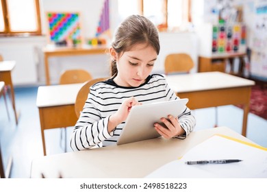 Portrait of cute schoolgirl sitting at desk using tablet during class, learning with technology. Student girl in classroom at the elementary school - Powered by Shutterstock