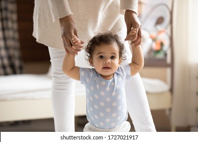 Portrait Of Cute Small African American Baby Girl Learn Walking At Home Holding Mom Hands, Little Biracial Toddler Infant Child Make Do First Steps With Mother Support, Childcare, Upbringing Concept