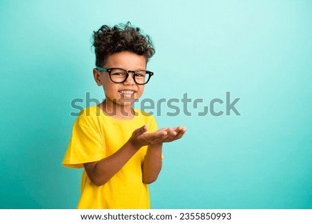 Portrait of cute small boy with brown hair wear stylish t-shirt in glasses hold product empty space isolated on teal color background