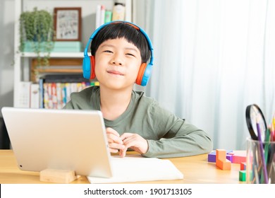 Portrait of a cute and smart asian student boy wearing headphone looking at camera and smile, he using tablet computer to join online classroom from home during Covid-19 pandemic lockdown. New normal.