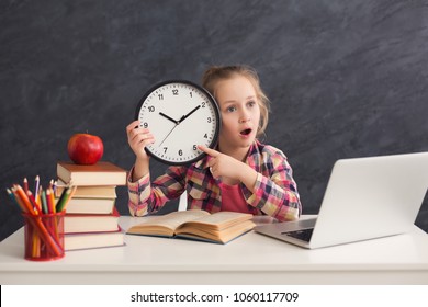 Portrait Of Cute Smart Girl Sitting With Stack Of Books And Laptop, Holding Big Clock And Pointing On It. Education, Development, Time Management, Deadline, Time To Study, School Concept