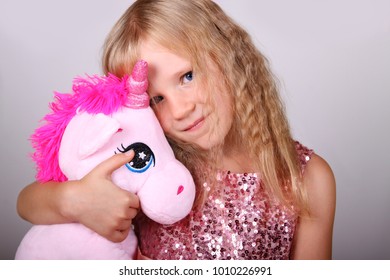 Portrait of cute smiling blond little girl in beautiful dress with pink plush unicorn