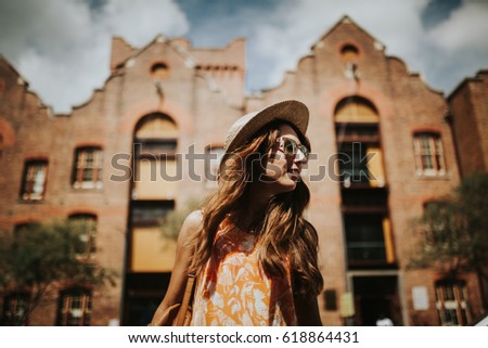 Happy thin woman with sunglasses and hat smiling while visiting The Rocks in Sydney city, Australia.