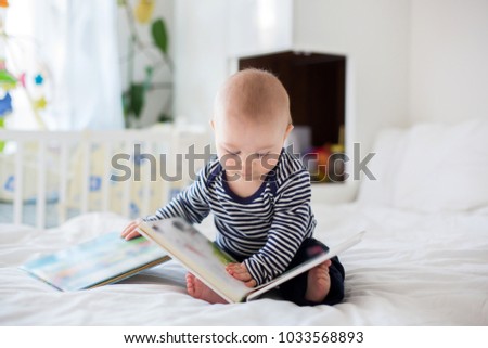 Portrait of a cute smiling infant baby boy reading a book. Happy childhood concept.