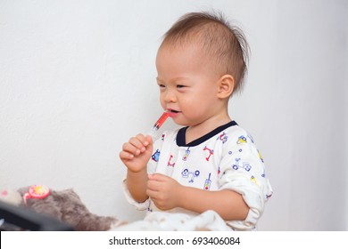 Portrait Of Cute Smiling Little Asian 18 Months / 1 Year Old Toddler Baby Boy Child Who Having Flu Feeding Himself With Liquid Medicine With A Syringe, Fever Cold And Flu Concepts