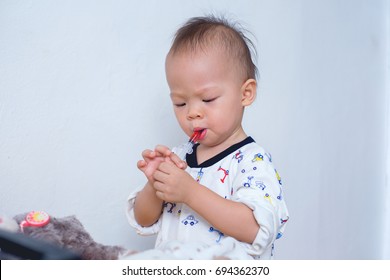 Portrait Of Cute Smiling Little Asian 18 Months / 1 Year Old Toddler Baby Boy Child Who Having Flu Feeding Himself With Liquid Medicine With A Syringe, Fever Cold And Flu Concepts