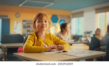 Portrait of a Cute Smiling Redhead Girl Sitting Behind a Desk in Class in Elementary School. Young Pupil is Looking at Camera, Smiling. Kids Educated in Modern Primary School - Powered by Shutterstock