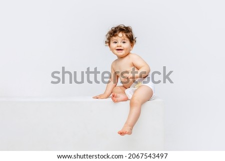Portrait of cute smiling toddler boy, baby in diaper sitting isolated over white studio background. Happy child. Concept of childhood, motherhood, life, birth. Copy space for ad