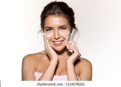 Portrait of cute smiling woman with foaming cleanser. Attractive joyful brunette looking at camera with happiness. Perfect fresh clean skin concept. Isolated on grey background