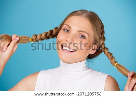 Portrait of cute smiling woman holding long hair pigtails on blue background.