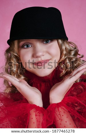 portrait of cute teenage girl. child in a black hat in a dress with red sleeves. retro style. pink background