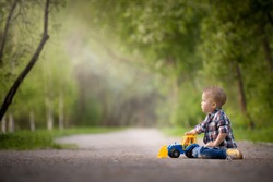 Portrait Of Cute Toddler Boy Sitting On The Ground And Playing With Toy Tractor And Sand In The Park. Child Walking Outdoors. Lifestyle.