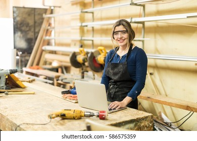 Portrait Of A Cute Woman Doing Some Work In A Woodshop And Using Reviewing A Design In A Laptop