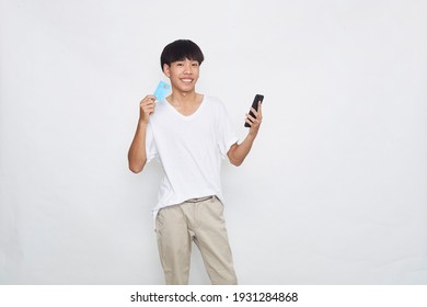 Portrait Of A Cute Young Asian Man Holding Mobile Phone And Showing Credit Card Isolated White Background