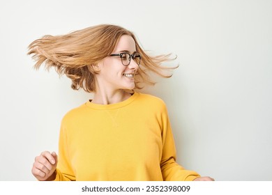 Portrait of cute young blond girl in glasses and yellow sweater shakes her head and plays with hair isolated on white studio background - Powered by Shutterstock