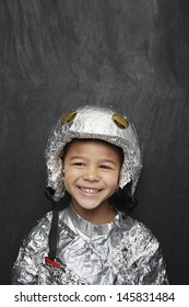 Portrait of a cute young boy in aluminum foil astronaut costume smiling against black background
