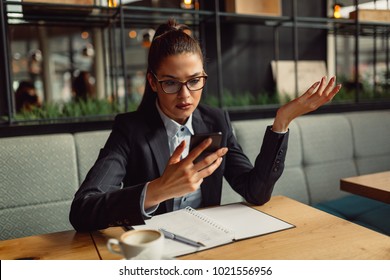 Portrait Of Cute Young Confused Business Woman Using Smartphone And Looking At The Screen.