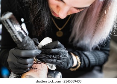 Portrait Of A Cute Young Female Tattoo Master Tattooing A Spider On The Girl's Forearm - Tattoo Artist Holding A Tattoo Machine In Sterile Black Gloves And Working In A Professional Studio