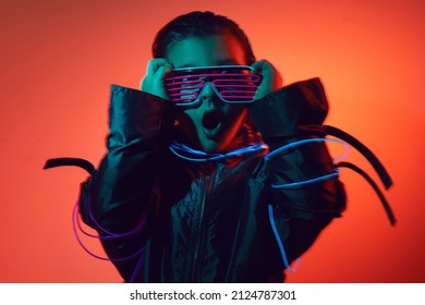 portrait cyberpunk boy child in neon glasses in blue and red tones with wires on a red background. Game, virtual reality. Future technologies.
