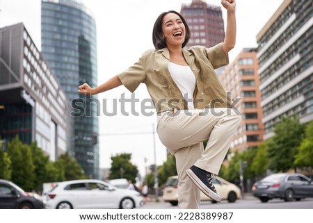 Portrait of dancing asian woman, raising hands up and feeling happy, posing in city, triumphing, feeling joy. Copy space