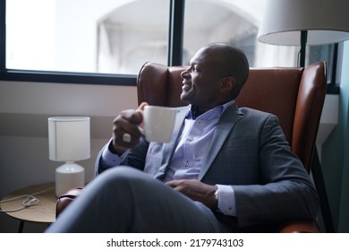 Portrait Of A Dapper Mature Hairless Black Man Entrepreneur, In A Custom Elegant Grey Costume, Sitting In An Outdoor Cafe On A Rainy Day And Pensively Looking Into The Distance