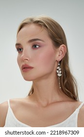 Portrait of a dark blond lady with gentle makeup. The attractive girl is wearing golden earrings with pendants made as white flowers and beads and posing on the light background. - Shutterstock ID 2218967309