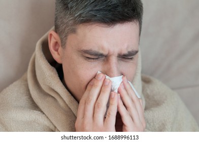 Portrait Of Dark Haired Ill Man Sniff Into Napkin Wrapped In A Blanket On Couch