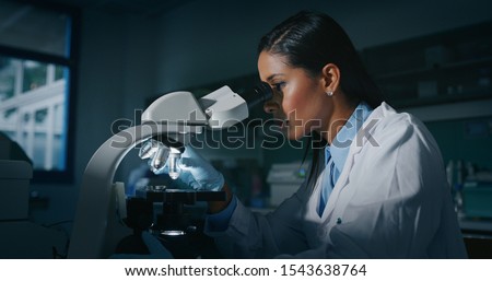 Portrait of dark skin female scientist is analyzing a sample to extract the DNA and molecules with microscope in laboratory.