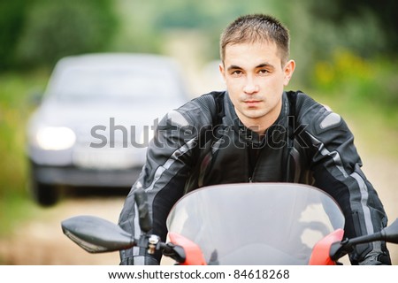Portrait of dark-haired man wearing leather jacket driving red motorcycle.