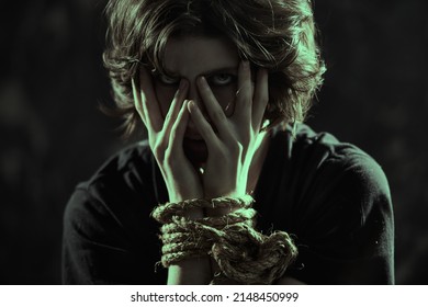 Portrait of a dark-haired woman holding her face with tied hands and looking at the camera with hatred. Violence against people, abusive treatment.