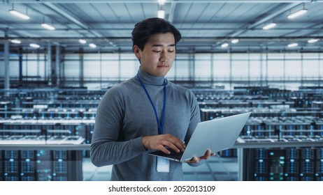 Portrait of a Data Center Engineer Using Laptop Computer. Server Room Specialist Facility with Korean Male System Administrator Working with Data Protection Network for Cyber Security.