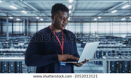 Portrait of a Data Center Engineer Using Laptop Computer. Server Room Specialist Facility with African American Male System Administrator Working with Data Protection Network for Cyber Security.