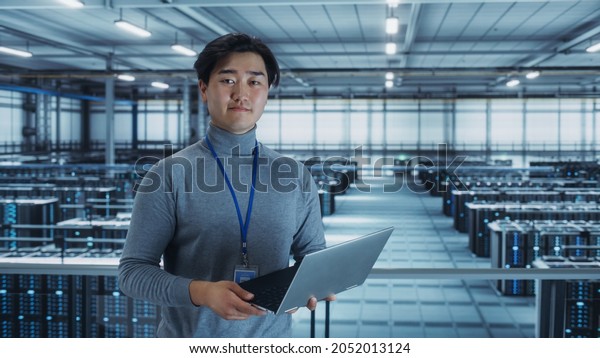 Portrait\
of a Data Center Engineer Using Laptop Computer. Server Room\
Specialist Facility with Korean Male System Administrator Working\
with Data Protection Network for Cyber\
Security.
