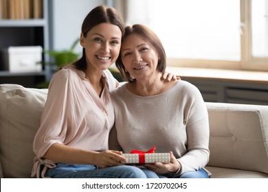 Portrait Daughter Hugging And Congratulating Older Mother With Birthday, Mothers Day Or 8 March, Happy Young Woman And Mature Mom Holding Gift Box, Looking At Camera, Sitting On Couch At Home