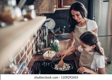 portrait of daughter and mother frying mushrooms on the stove together for dinner at the kitchen