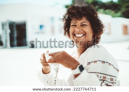 Portrait of a dazzling happy plus-size mature Hispanic female with curly hair and white a perfect smile, laughing while drinking tea in an outdoor cafe on a sunny day; a copy space area on the left
