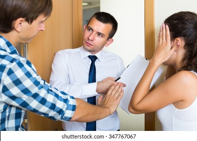 Portrait Of Debt Collector And Young Spouses With Overdue Payment At The Doorway