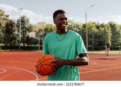 Portrait of delighted african american basketball player guy standing at basketball court with ball smiling laughing spending time with company showing skills trying to make slam dunk. - Powered by Shutterstock