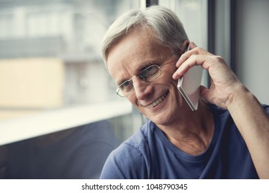 Portrait of delighted male person in old age holding cellphone close to ear and looking at window - Powered by Shutterstock