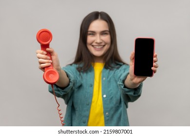 Portrait of delighted smiling woman holding out retro phone and cell phone, choose best device for you, wearing casual style jacket. Indoor studio shot isolated on gray background.