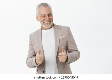 POrtrait Of Delighted And Successful Self-assured Old Handsome Man With Grey Beard And Moustache Winking And Smiling Showing Thumbs Up In Like Or Approval Gesture Giving Positive Feedback