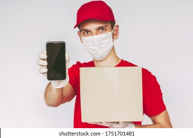 Portrait Delivery Guy In Protective Face Mask, Medical Glove Carry Mobile Phone, Parcel Box In Hand, Isolated Background. Man Delivery Service Courier Hold Smart Phone, Cardboard Box, Empty Copy Space