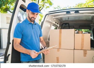 Portrait of a delivery man checking the products in checklist while standing right next to his van. Delivery and shipping concept.