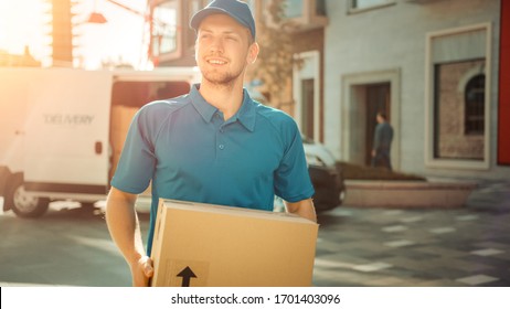Portrait of Delivery Man Holds Cardboard Box Package Standing in Modern Stylish Business District with Delivery Van in Background. Smiling Courier On Way to Deliver Postal Parcel to Client. Sun Flare